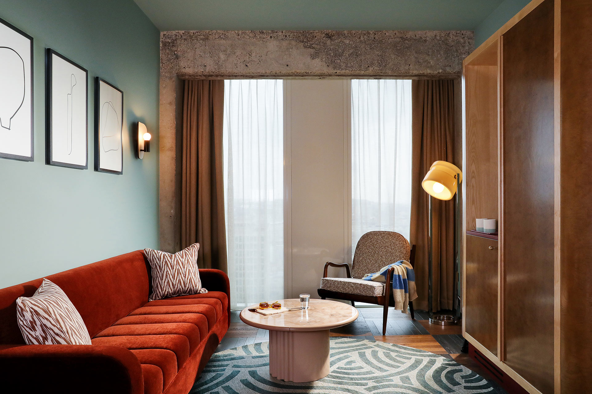 A red sofa, open wardrobe and chair lead the eye to the window with a view.